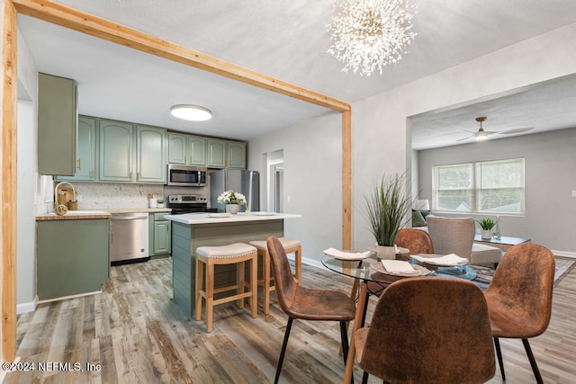 kitchen featuring ceiling fan with notable chandelier, a breakfast bar area, light hardwood / wood-style flooring, green cabinetry, and stainless steel appliances