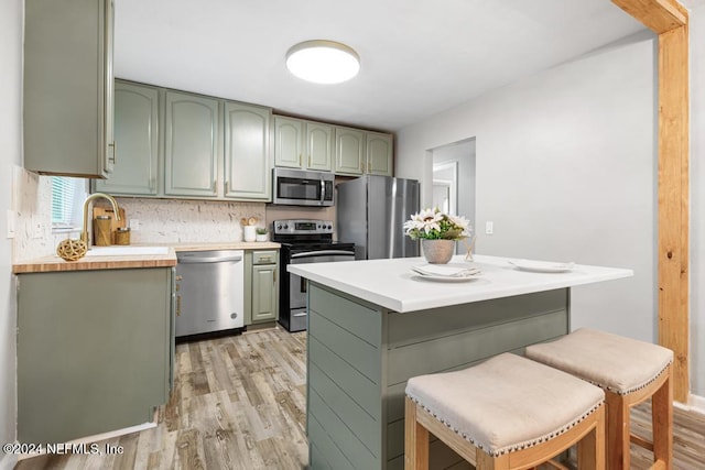 kitchen featuring tasteful backsplash, light hardwood / wood-style flooring, a breakfast bar, appliances with stainless steel finishes, and green cabinetry