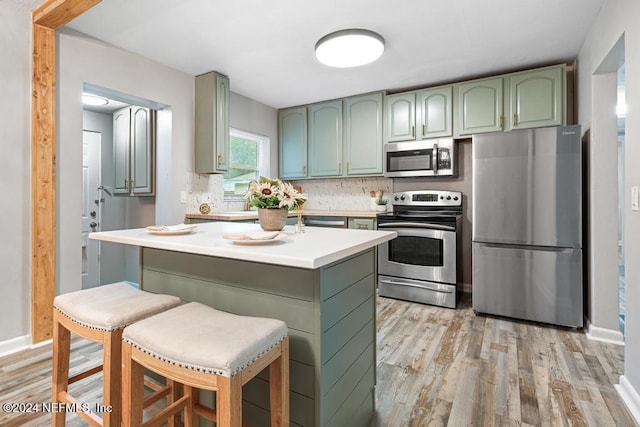 kitchen featuring appliances with stainless steel finishes, tasteful backsplash, green cabinetry, and a kitchen breakfast bar