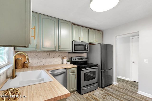 kitchen with wood counters, sink, green cabinetry, light wood-type flooring, and stainless steel appliances