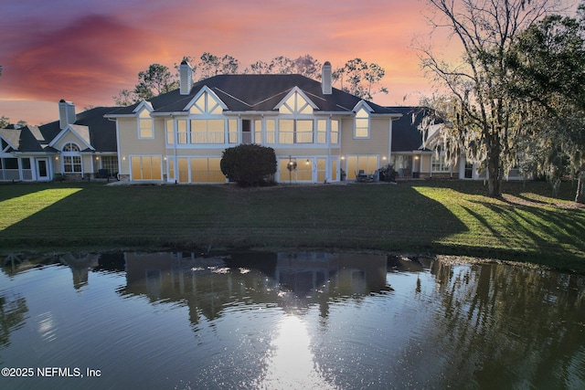 back house at dusk with a water view and a lawn