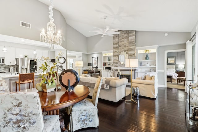 dining room with dark hardwood / wood-style flooring, built in shelves, ceiling fan with notable chandelier, a tile fireplace, and high vaulted ceiling