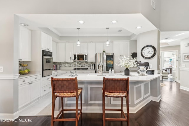 kitchen with white cabinets, appliances with stainless steel finishes, hanging light fixtures, and a kitchen island with sink