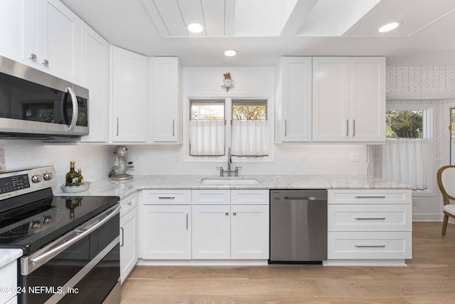 kitchen featuring light stone countertops, appliances with stainless steel finishes, white cabinetry, and sink