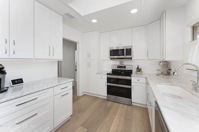 kitchen featuring sink, light stone countertops, light hardwood / wood-style floors, white cabinetry, and stainless steel appliances