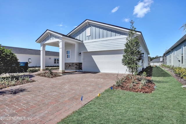 view of front of property featuring decorative driveway, an attached garage, board and batten siding, stone siding, and a front lawn