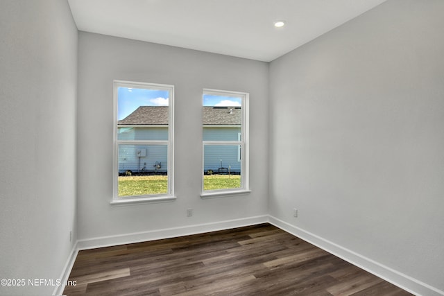 empty room featuring baseboards, dark wood finished floors, and a wealth of natural light