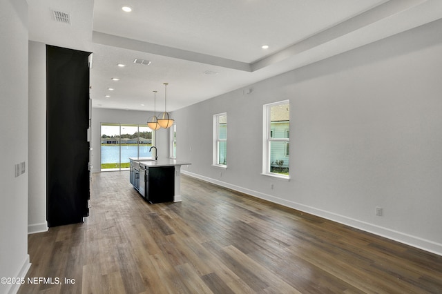 interior space with baseboards, visible vents, dark wood finished floors, a kitchen island with sink, and light countertops