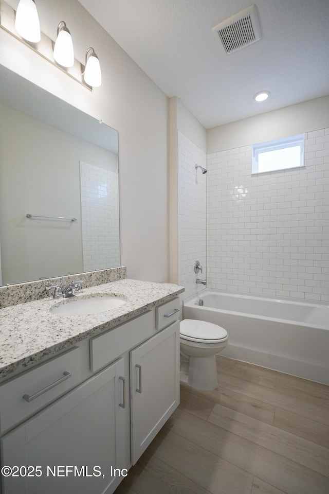 full bathroom with hardwood / wood-style flooring, tiled shower / bath combo, toilet, and vanity