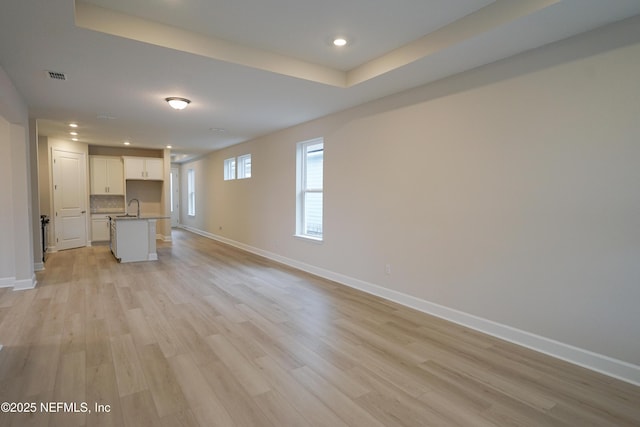 unfurnished living room with a raised ceiling, sink, and light wood-type flooring