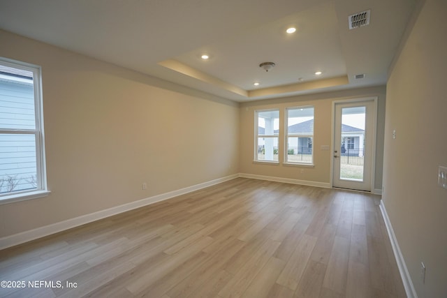 spare room with baseboards, visible vents, a tray ceiling, light wood-style floors, and recessed lighting