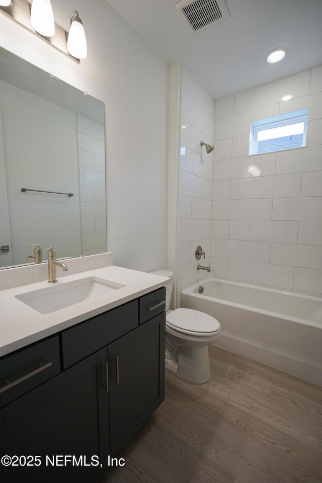 full bathroom with hardwood / wood-style floors, vanity, tiled shower / bath combo, and toilet