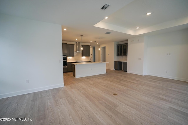 unfurnished living room with a raised ceiling, light hardwood / wood-style flooring, and sink