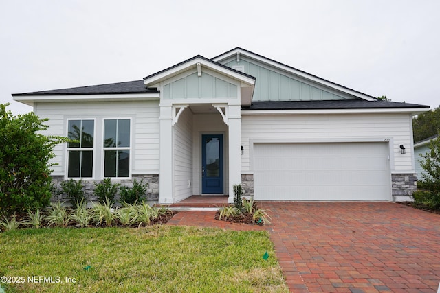 view of front of home with an attached garage, stone siding, decorative driveway, and board and batten siding