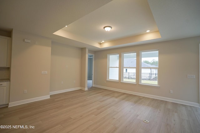 unfurnished room featuring light wood-type flooring, a raised ceiling, and baseboards