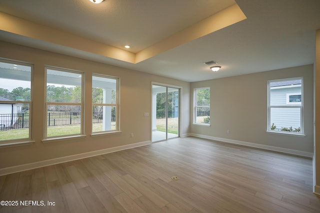 empty room with a tray ceiling, recessed lighting, visible vents, light wood-style flooring, and baseboards