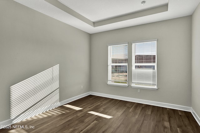 spare room with a tray ceiling, baseboards, and dark wood-type flooring