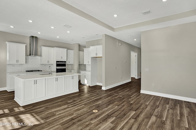 kitchen with a sink, visible vents, black appliances, wall chimney exhaust hood, and a center island with sink