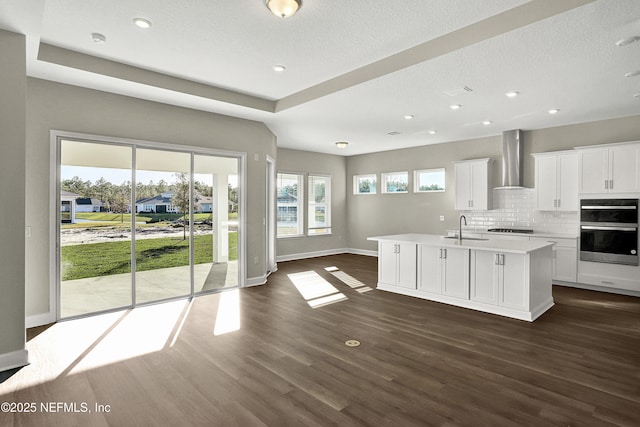 kitchen featuring cooktop, wall chimney exhaust hood, dark wood-type flooring, light countertops, and a sink