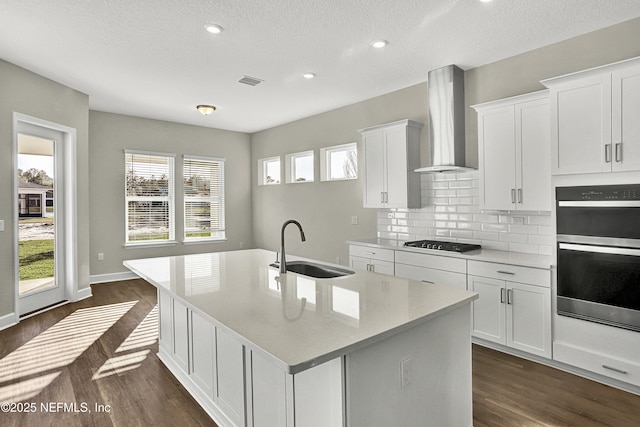 kitchen with double wall oven, a sink, gas stovetop, dark wood-style floors, and wall chimney exhaust hood