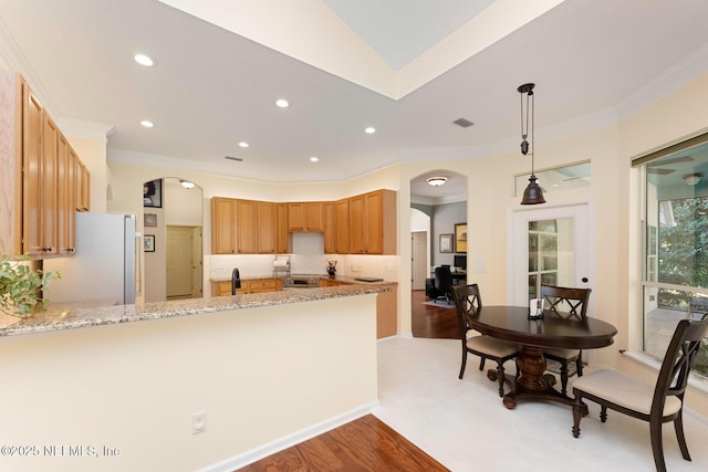 kitchen with kitchen peninsula, light stone counters, light hardwood / wood-style floors, white fridge, and hanging light fixtures