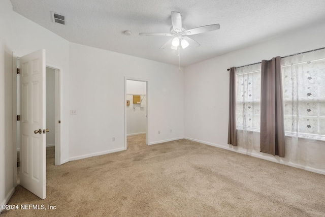 unfurnished bedroom with a textured ceiling, light colored carpet, a spacious closet, and ceiling fan