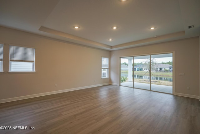 spare room with dark hardwood / wood-style flooring, a raised ceiling, and a water view