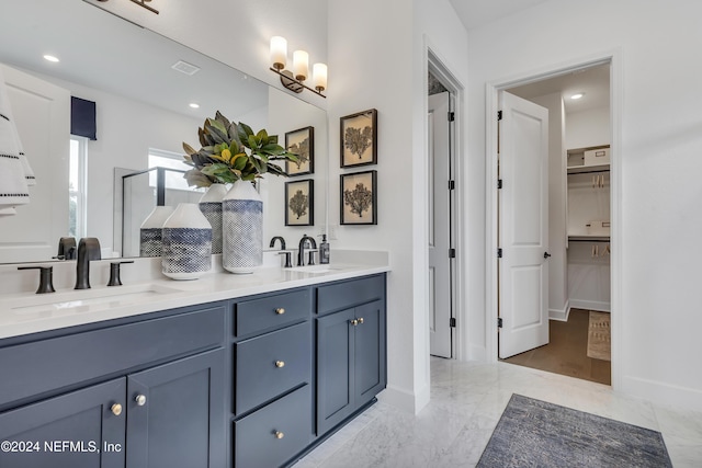 full bathroom with a walk in closet, marble finish floor, a sink, and double vanity