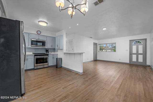 kitchen with decorative backsplash, appliances with stainless steel finishes, a textured ceiling, light hardwood / wood-style flooring, and a notable chandelier