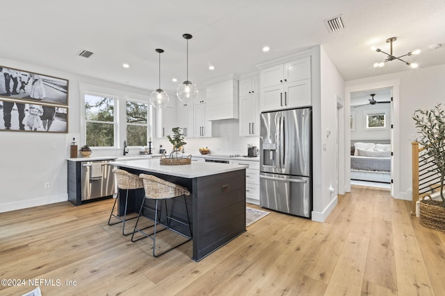 kitchen with appliances with stainless steel finishes, premium range hood, a kitchen island, white cabinetry, and decorative light fixtures