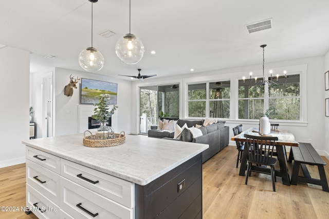 kitchen with decorative light fixtures, white cabinetry, a center island, light wood-type flooring, and ceiling fan with notable chandelier