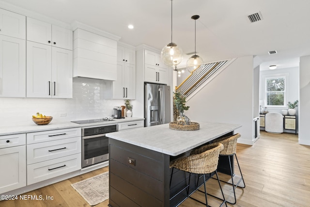 kitchen featuring stainless steel appliances, hanging light fixtures, a center island, decorative backsplash, and white cabinets