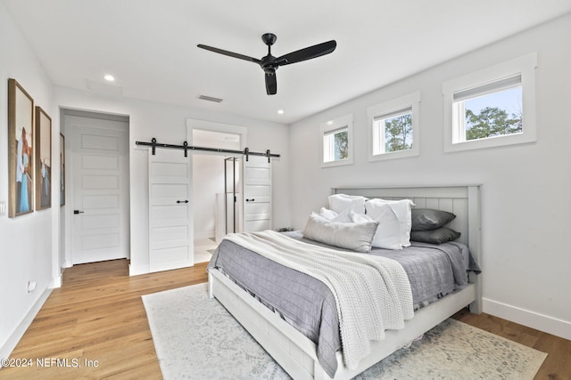 bedroom with ceiling fan, light wood-type flooring, connected bathroom, and a barn door