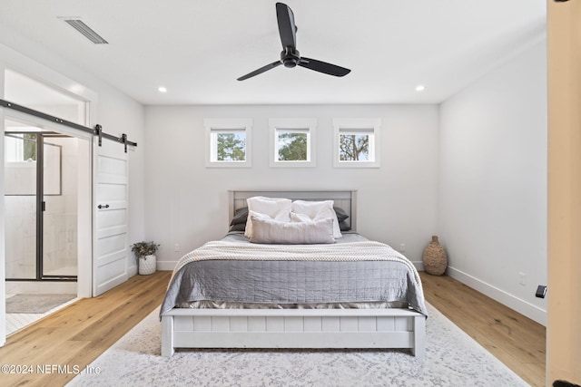 bedroom featuring connected bathroom, ceiling fan, hardwood / wood-style flooring, and a barn door