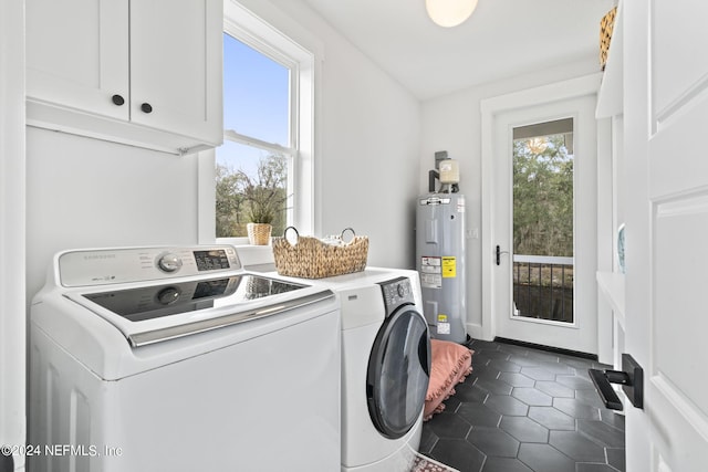 laundry area featuring water heater, washing machine and dryer, dark tile patterned flooring, and cabinets