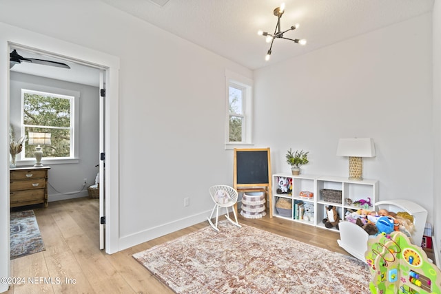 game room with ceiling fan with notable chandelier, a textured ceiling, and light hardwood / wood-style flooring