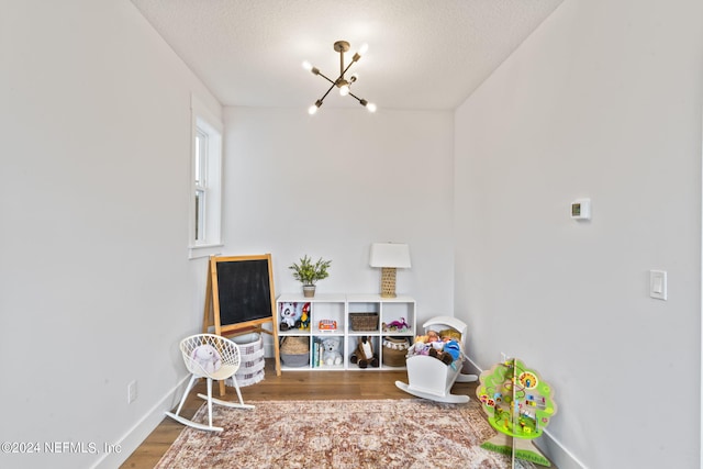 playroom with an inviting chandelier, a textured ceiling, and hardwood / wood-style floors