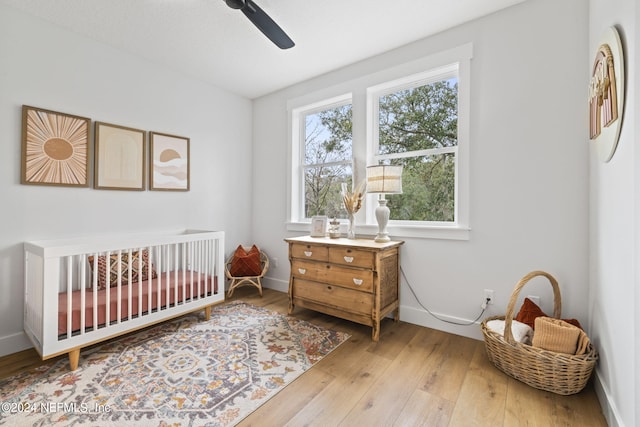 bedroom with a crib, ceiling fan, and light hardwood / wood-style flooring