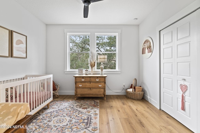 bedroom with a crib, a closet, ceiling fan, and light wood-type flooring