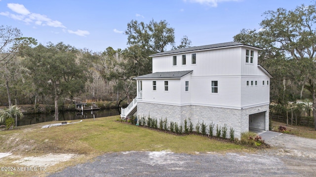 rear view of house with a garage, a water view, and a lawn