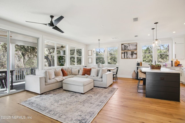 living room with light wood-type flooring and ceiling fan with notable chandelier