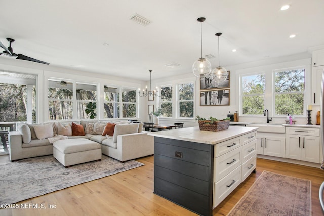 kitchen with light hardwood / wood-style floors, a kitchen island, white cabinets, decorative light fixtures, and sink