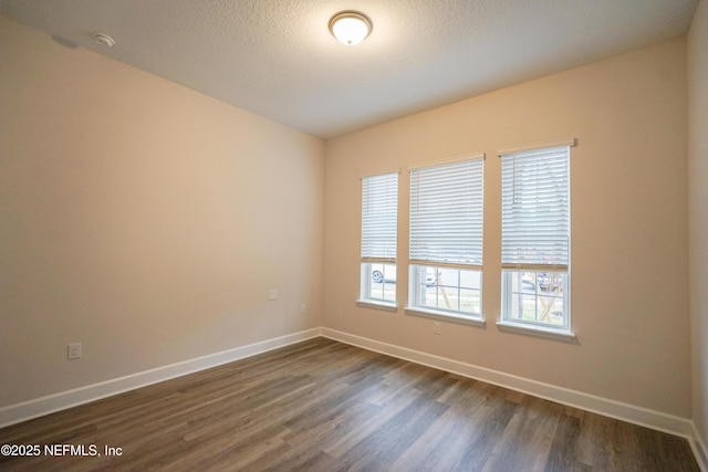 spare room featuring a textured ceiling, baseboards, and dark wood-type flooring