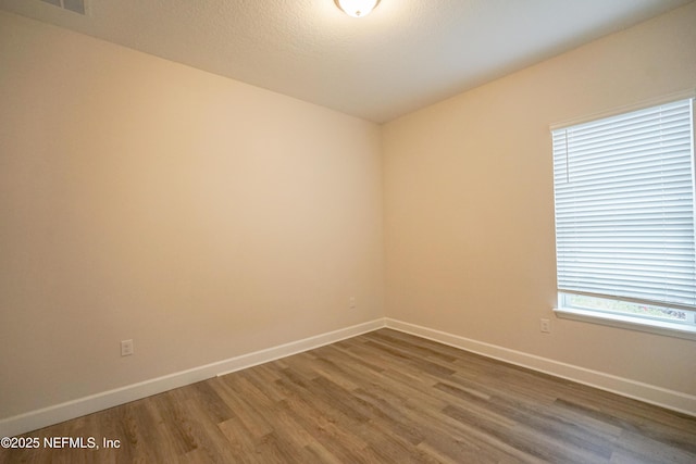 unfurnished room with a textured ceiling, baseboards, and wood finished floors