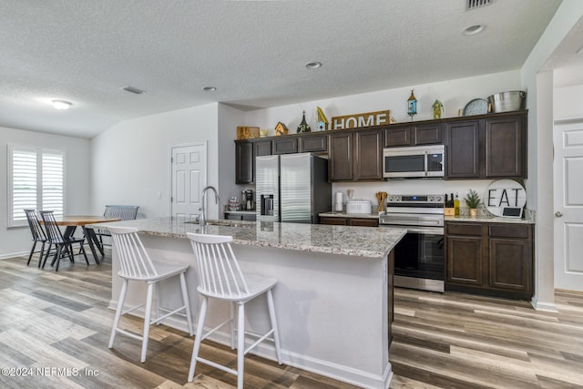 kitchen with a center island with sink, dark brown cabinets, a kitchen bar, and stainless steel appliances