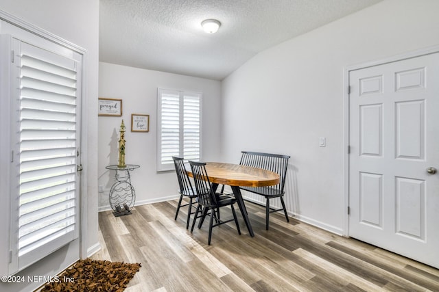 dining area with light hardwood / wood-style floors, a textured ceiling, and vaulted ceiling