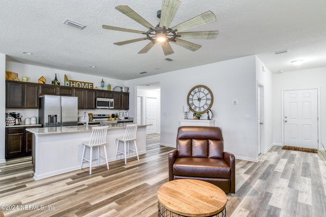 kitchen featuring light stone countertops, appliances with stainless steel finishes, light hardwood / wood-style floors, and a kitchen island with sink