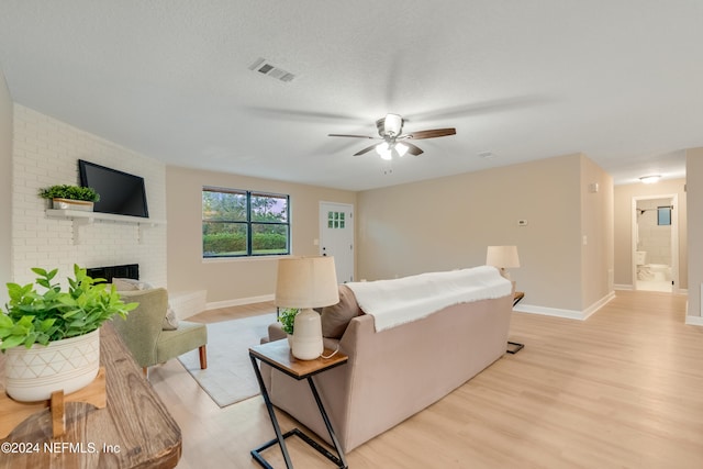 living room with ceiling fan, a fireplace, light hardwood / wood-style floors, and a textured ceiling