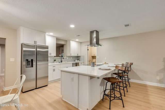 kitchen with sink, island exhaust hood, decorative backsplash, white cabinets, and appliances with stainless steel finishes