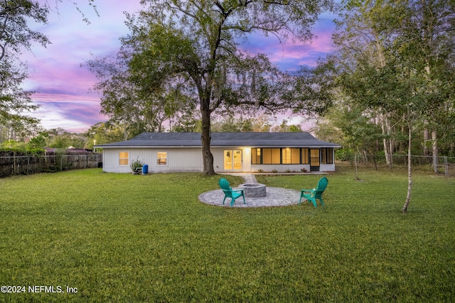 back house at dusk featuring a fire pit, a sunroom, a patio area, and a lawn